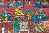 Wat Xieng Thong temple in Luang Prabang, Laos.  La Chapelle Rouge , the Red Chapel. The exterior walls are decorated with colourful mosaics on a pink background with scenes of people daily activities. South wall.